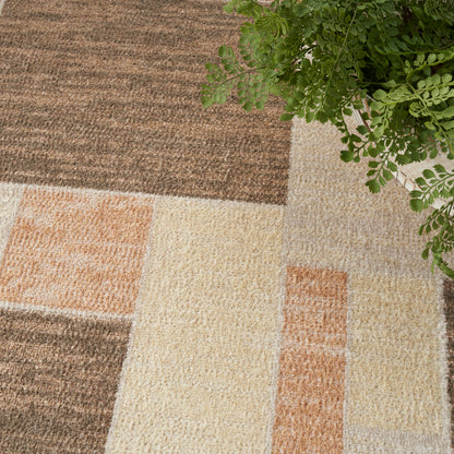 Patchwork shag rug in brown, beige, cream and peach tones with a green plant in the top corner.