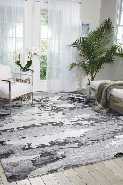 Plush abstract gray, black & white area rug in a bright living room with white furniture & green plants.