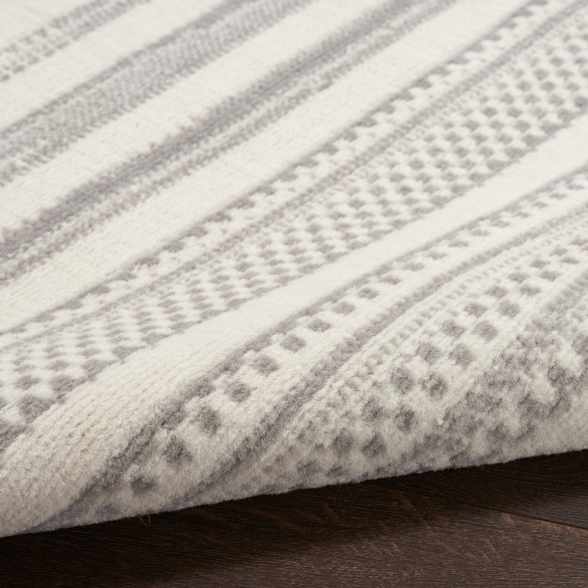 Light gray and white striped woven rug with dotted geometric pattern, wool-like texture on wooden floor.