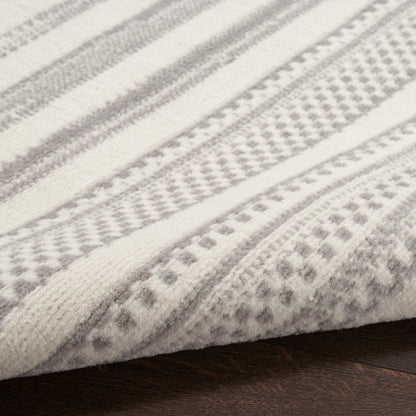 Light gray and white striped woven rug with dotted geometric pattern, wool-like texture on wooden floor.