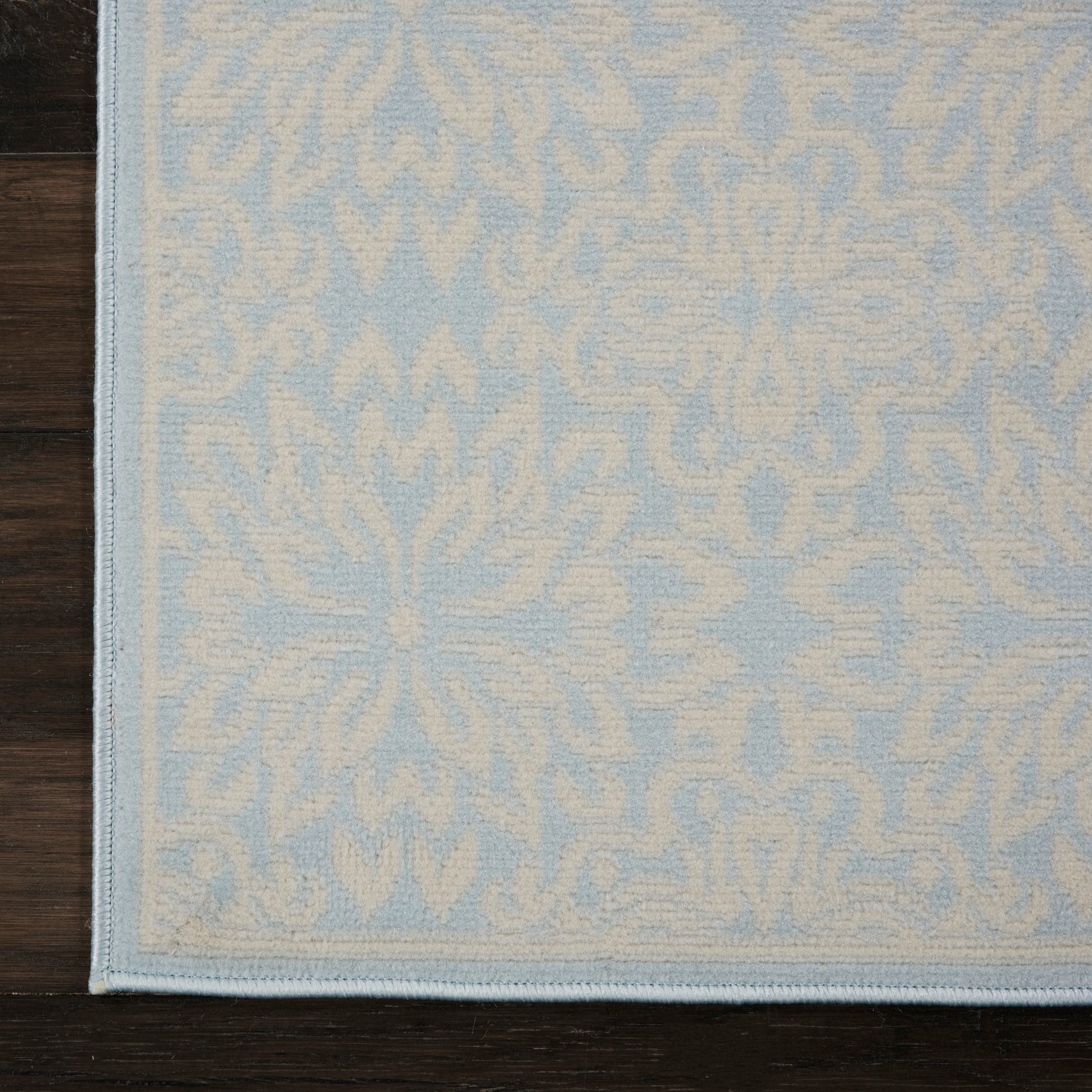 Light blue rug with white damask pattern and pale border on dark wooden floor.