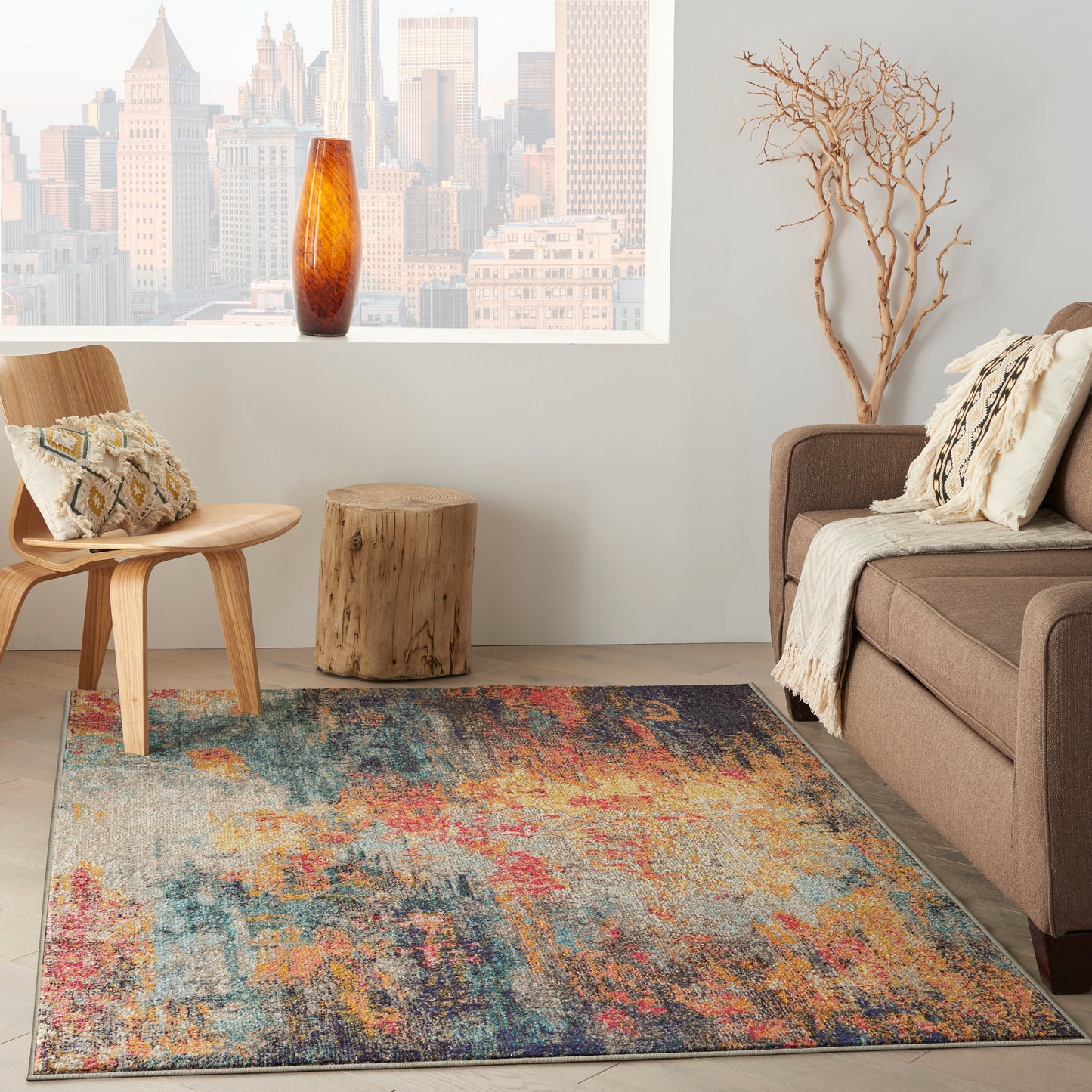 Rectangular colorful abstract area rug in a modern living room with beige sofa, wooden chair and amber vase by city window