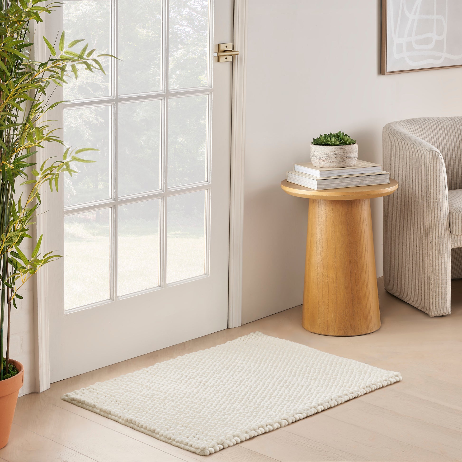 Neutral 2' x 3' rug in a cozy living space; light beige rug with a round wooden side table, books and a plant nearby.
