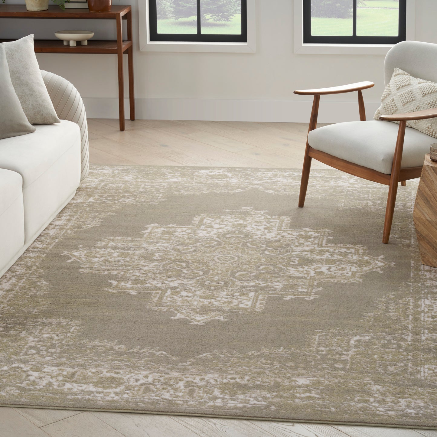 Neutral living room with taupe geometric patterned area rug, white sofa with gray pillows, and mid-century wooden armchair.