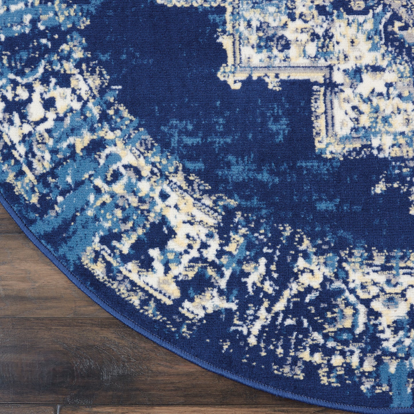 Round navy blue area rug with distressed abstract pattern in light blues and cream, bound edge on wood floor.
