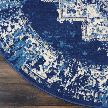 Round navy blue area rug with distressed abstract pattern in light blues and cream, bound edge on wood floor.
