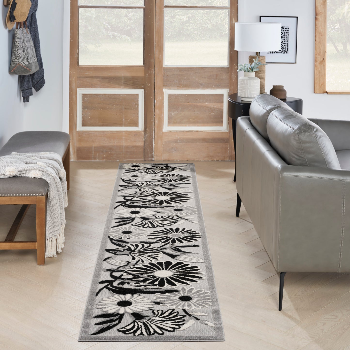 Long floral runner rug with black petals on light gray, laid in a cozy living area between a bench and gray sofa.