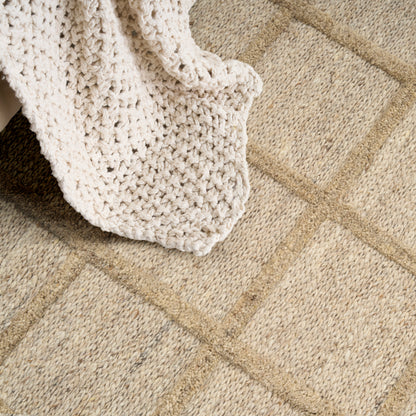 Cream chunky knit blanket draped over a beige geometric square-pattern rug.