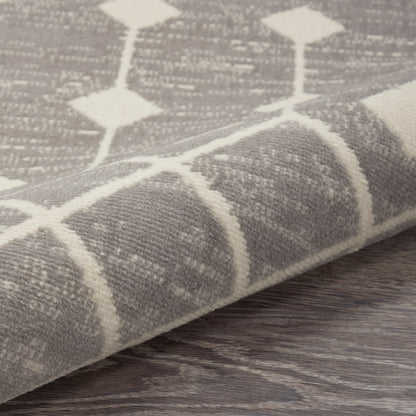 Gray woven rug with white diamond lattice pattern, folded edge on dark wood flooring.