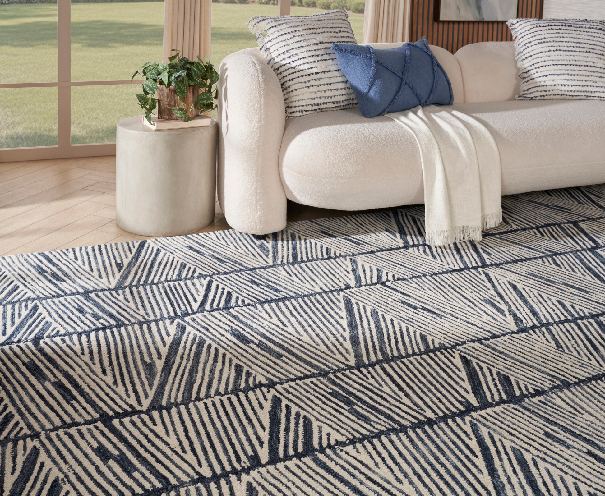Cream sofa with blue cushions and beige throw; navy geometric area rug with diagonal line triangles in a modern living room.