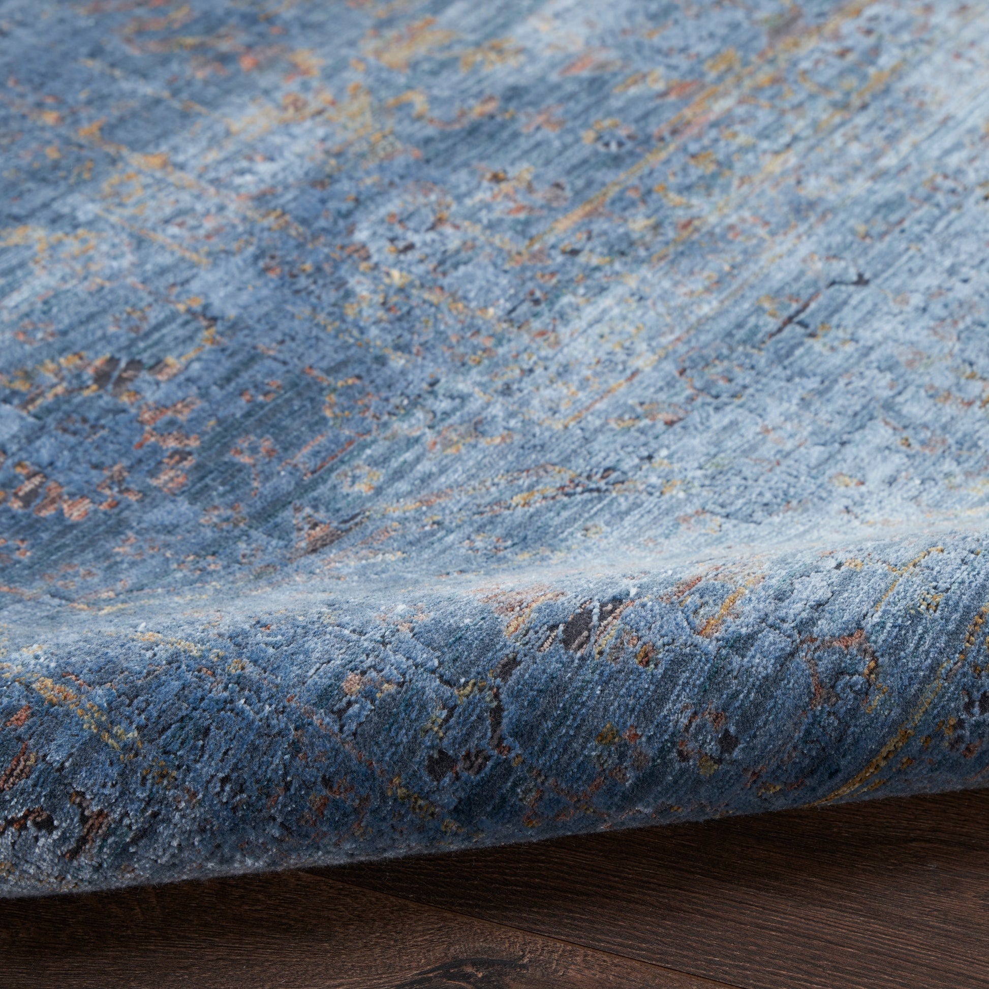 Blue distressed oriental rug with gold & brown floral motifs, plush pile, partially folded over dark wood floor.