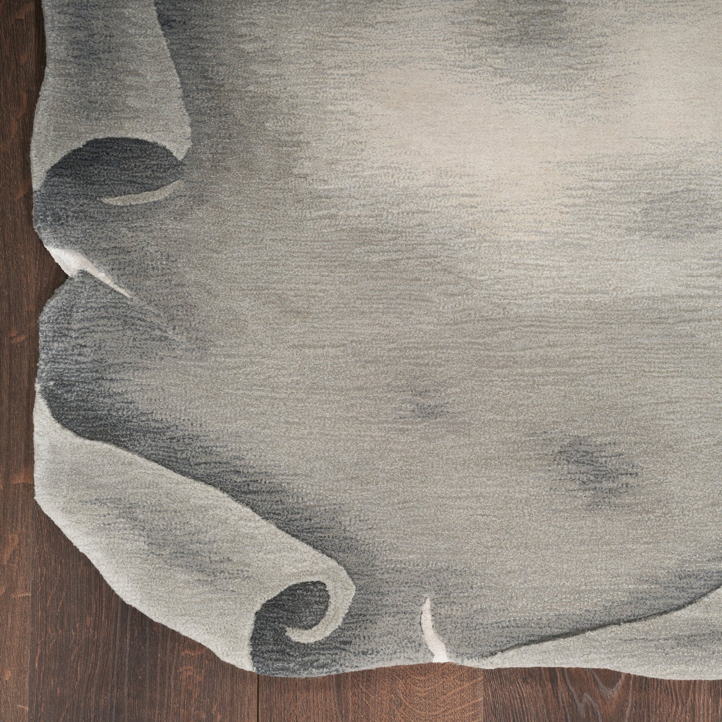 Light gray textured rug with rolled corner on dark wood floor.