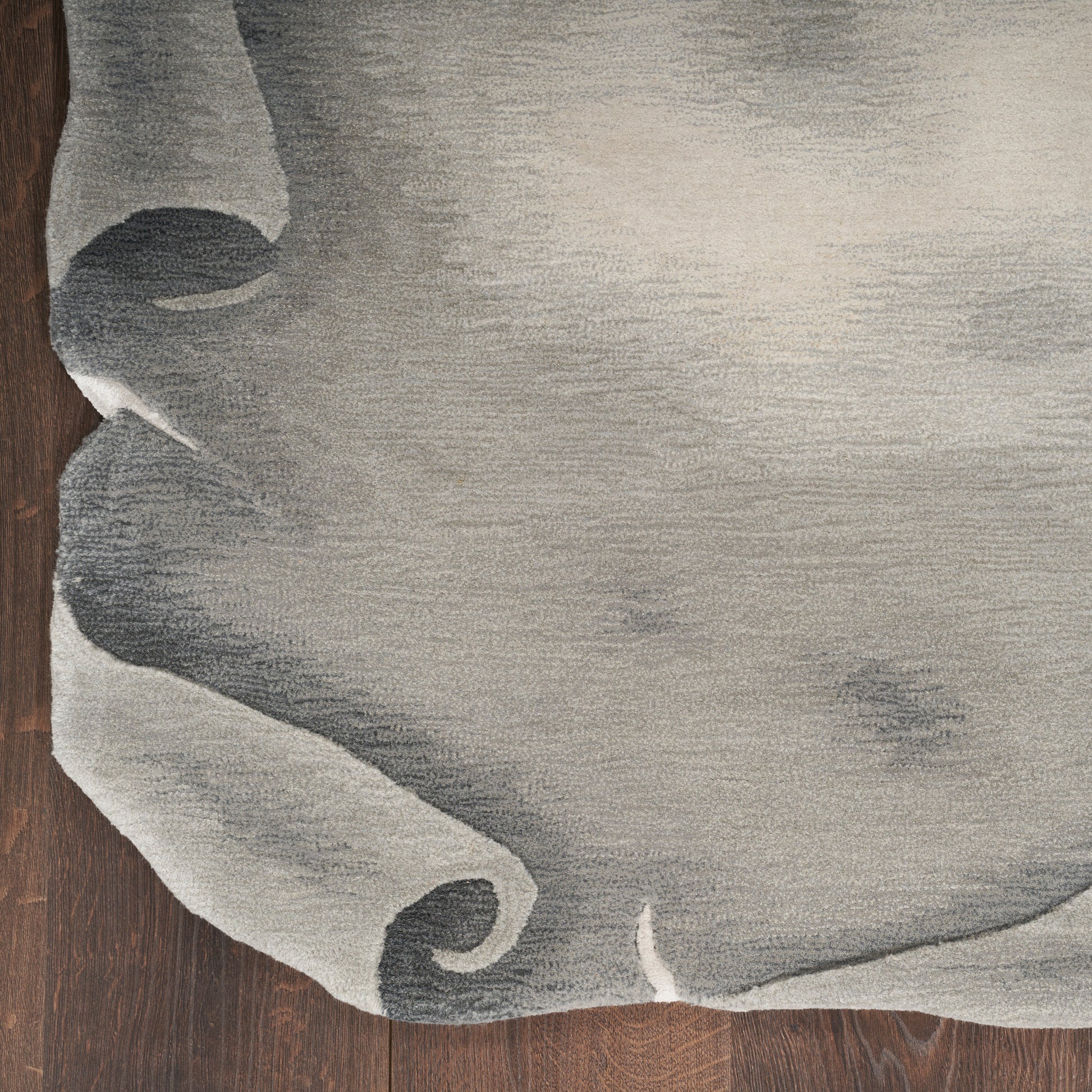 Light gray textured rug with rolled corner on dark wood floor.