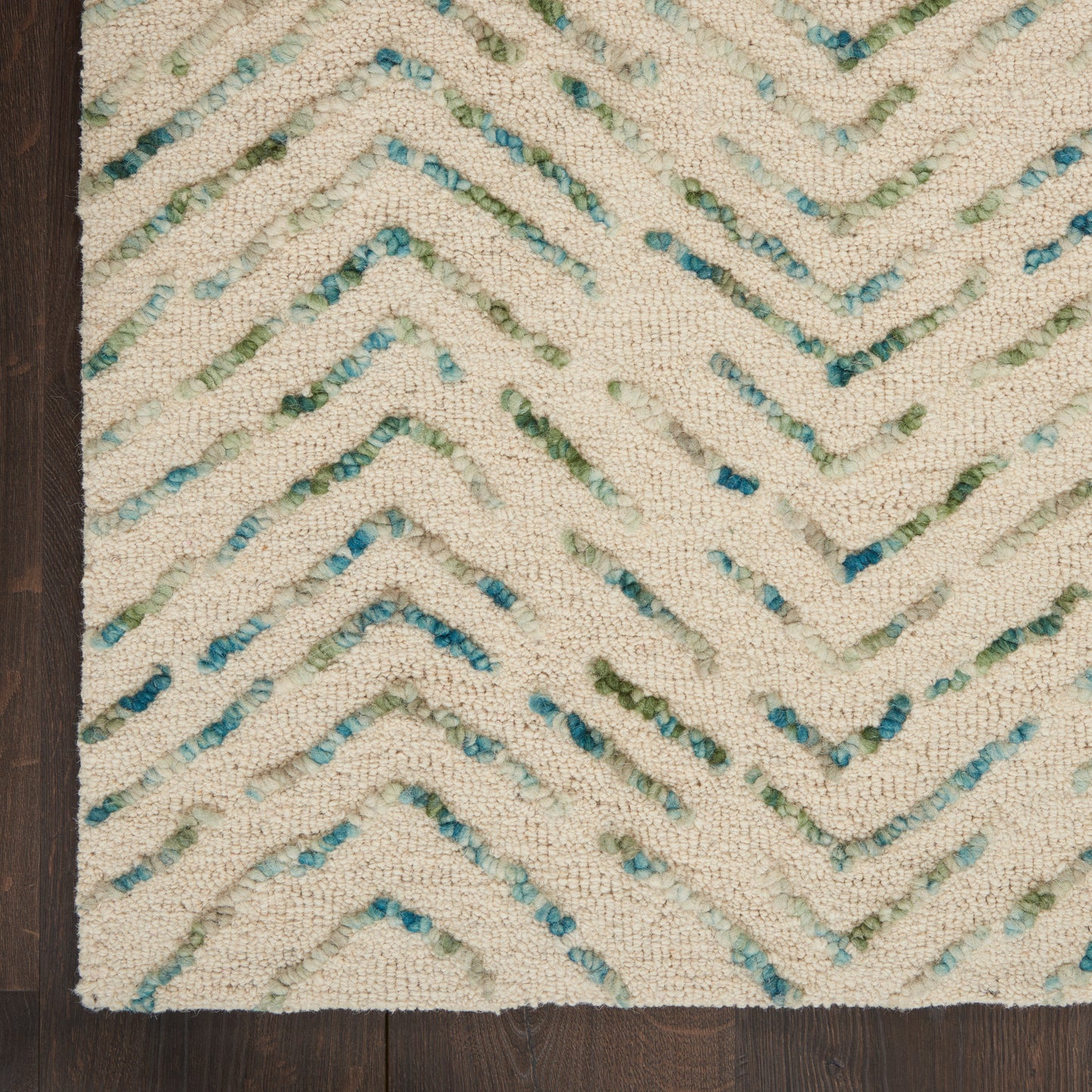 Cream textured shag rug with turquoise and green chevron zigzag pattern on dark hardwood floor.