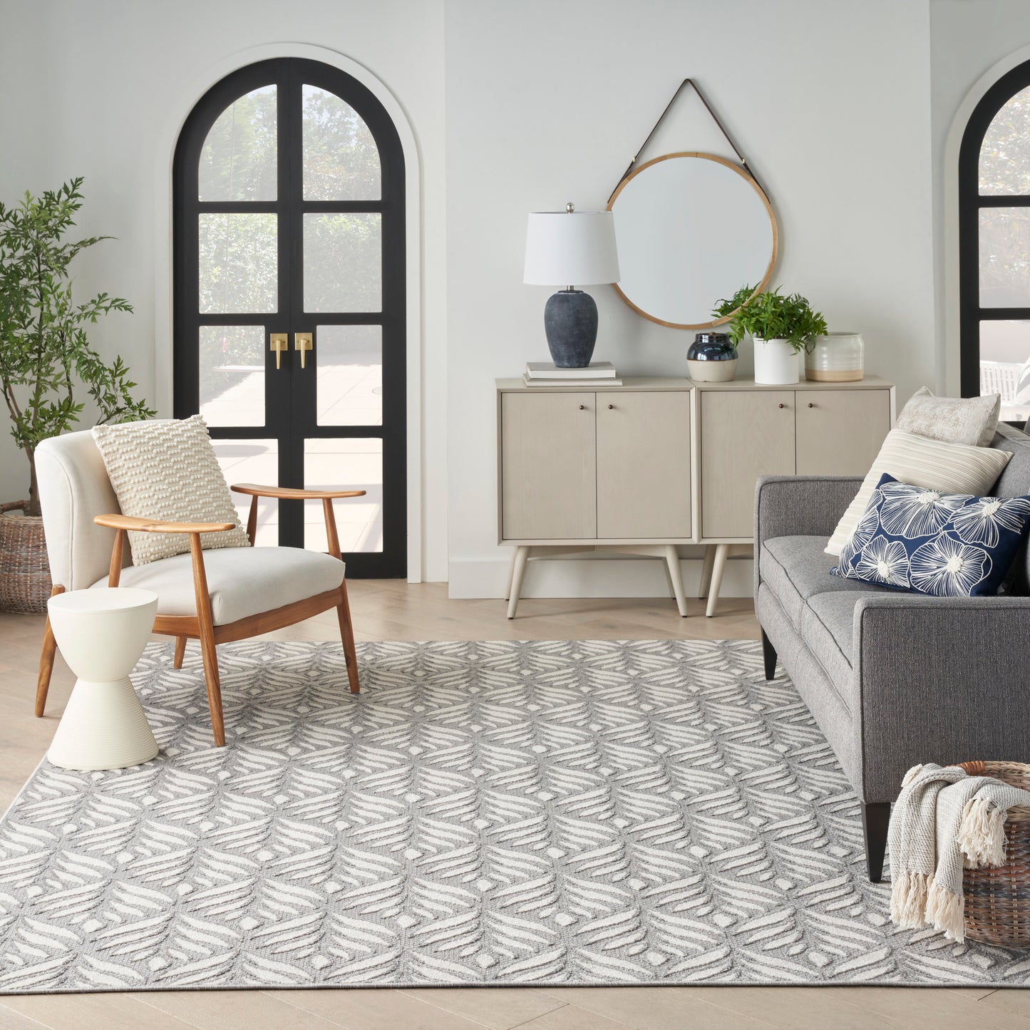 Cozy living room with arched doors, beige console, mirror, blue lamp, plants, gray sofa, wood chair, tropical rug.