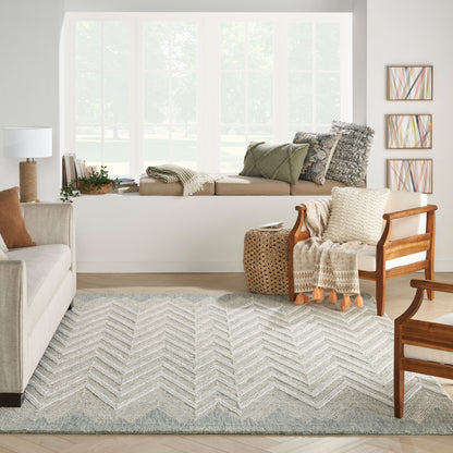 Cozy living room with window seat, beige sofa, wooden chairs, chevron rug, knit throw, wicker table, and abstract art.