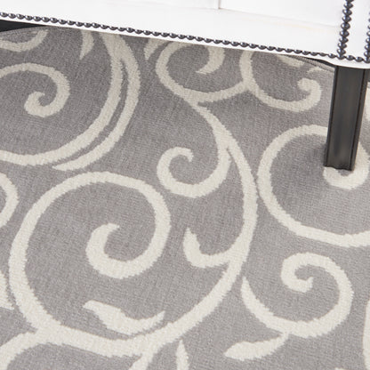 Gray rug with cream scrolling damask pattern; white upholstered chair edge with nailhead trim and black leg.