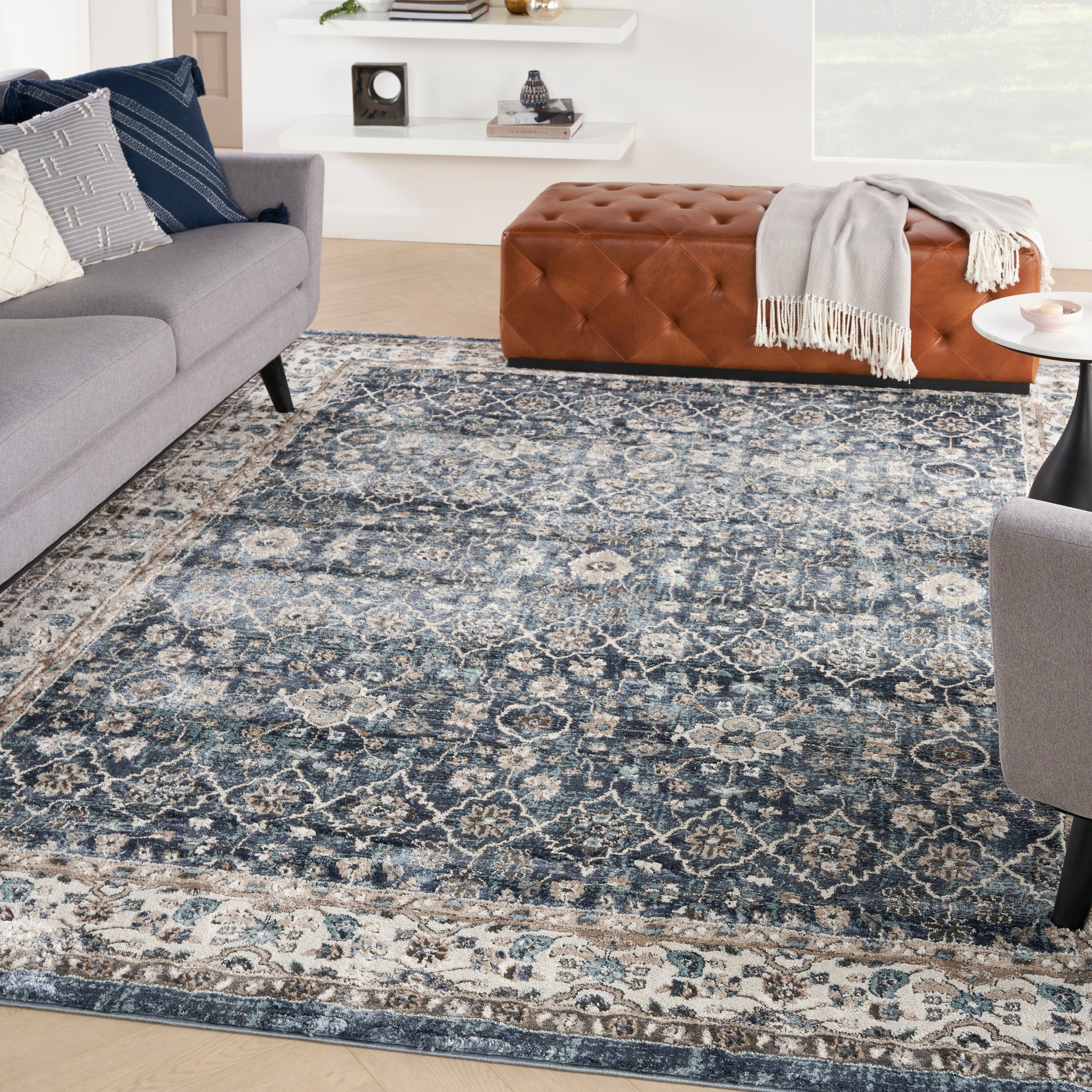 Living room with a blue distressed oriental rug, tufted brown leather ottoman, gray sofa with navy/white pillows.