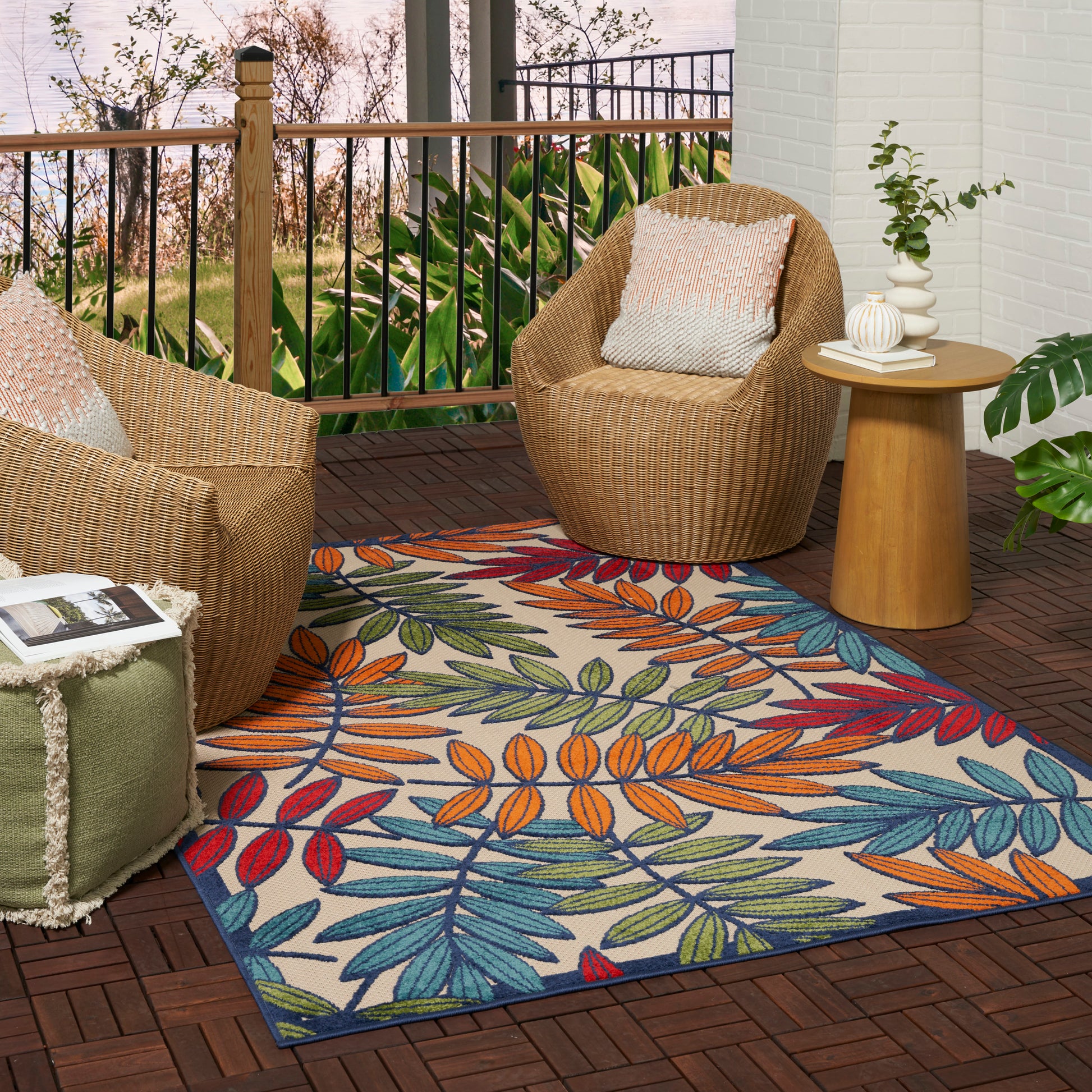 Tropical leaf-pattern rug on a brown deck, with outdoor wicker chairs around a round wooden table.