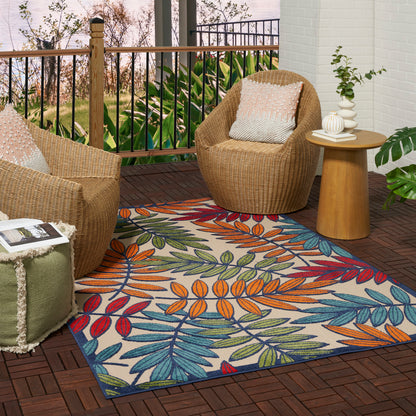 Tropical leaf-pattern rug on a brown deck, with outdoor wicker chairs around a round wooden table.