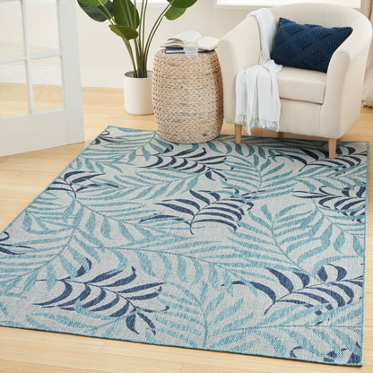 Teal and navy tropical leaf rug on light wood floor beside a cream armchair with navy cushion.