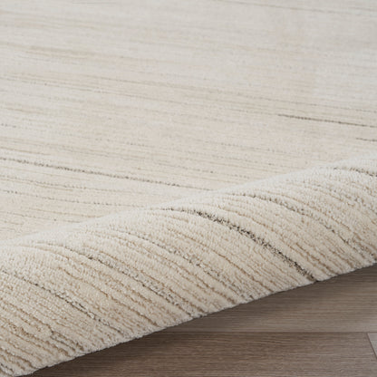 Cream beige shag rug with subtle linear stripes and plush pile, curled edge on light wood flooring.