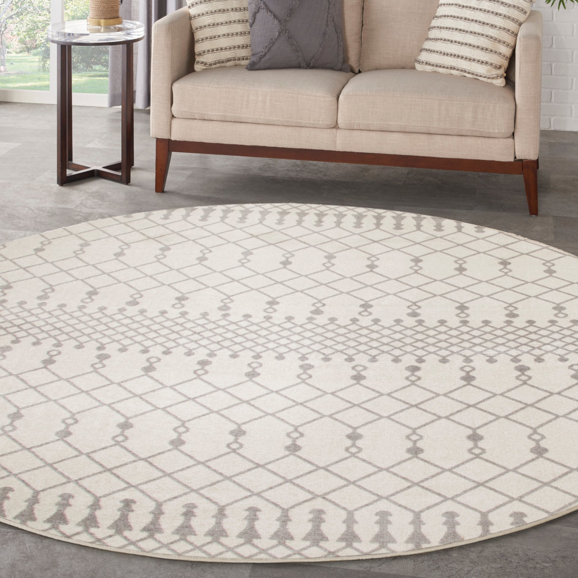 Round beige rug with gray lattice pattern under a beige sofa with striped cushions and a glass-top side table.