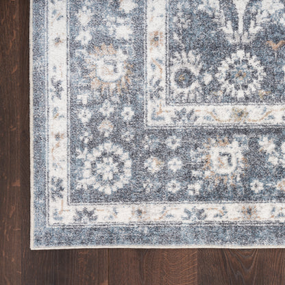 Blue and ivory patterned rug with floral motifs and borders on dark wood floor.