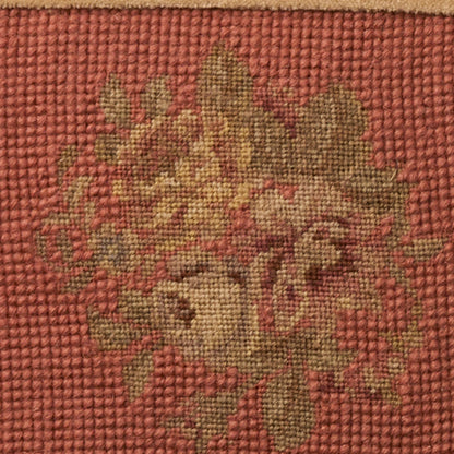 Close-up of a woven tapestry rug featuring a green-beige floral motif on a red textured background.