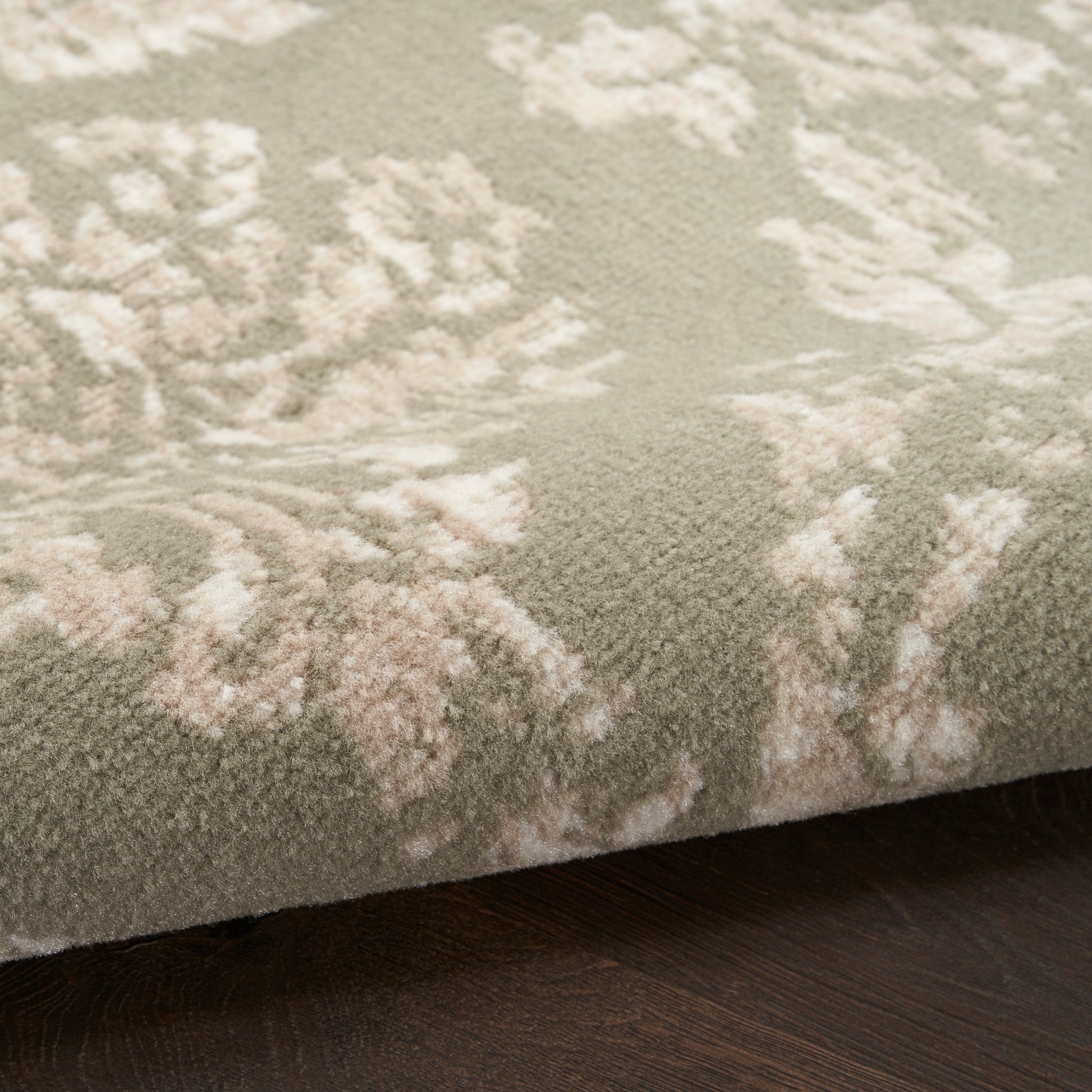 Close-up of a plush taupe rug with pale pink floral damask pattern on dark wood floor.