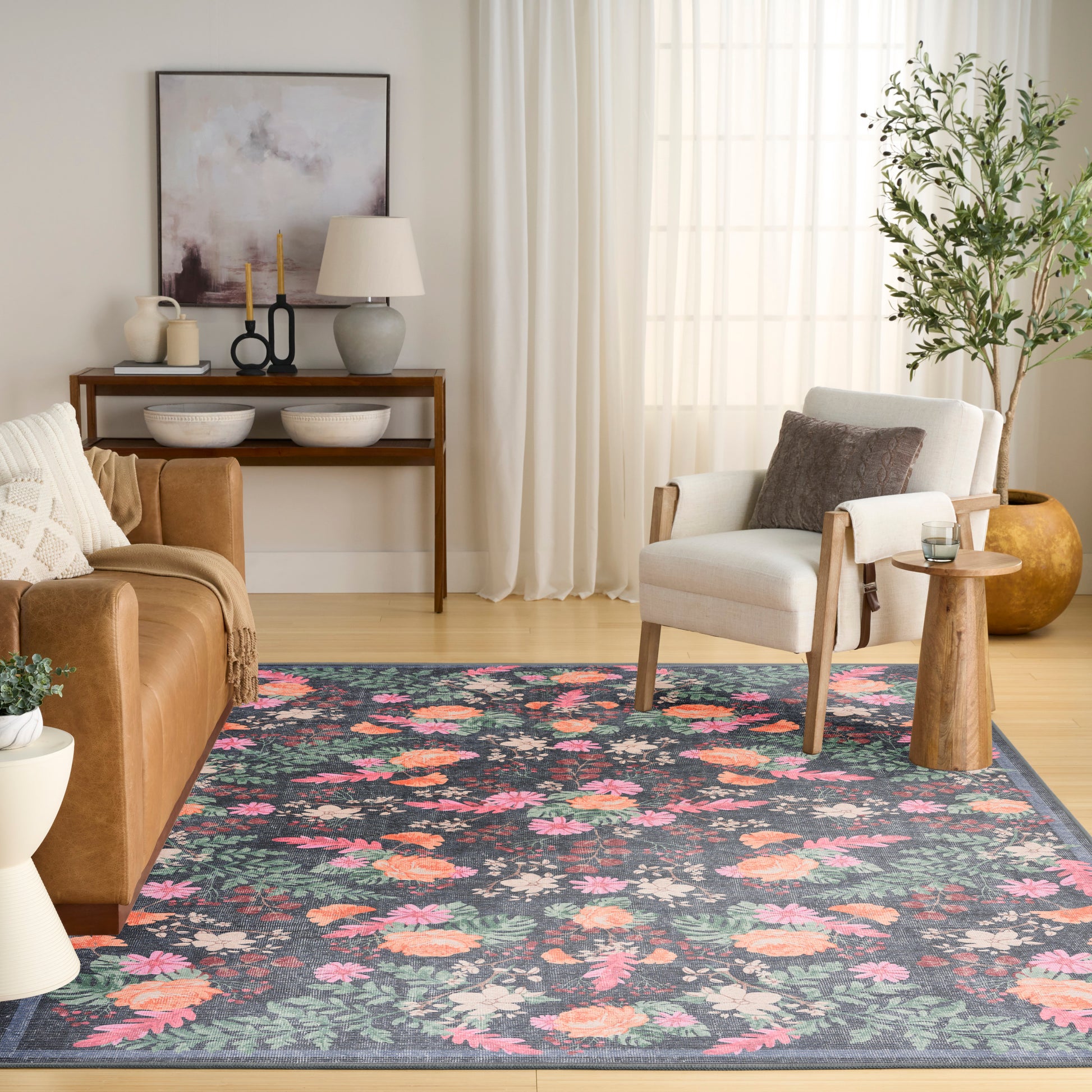 Floral area rug with pink and orange flowers on teal background in a bright living room with leather sofa and cream armchair.
