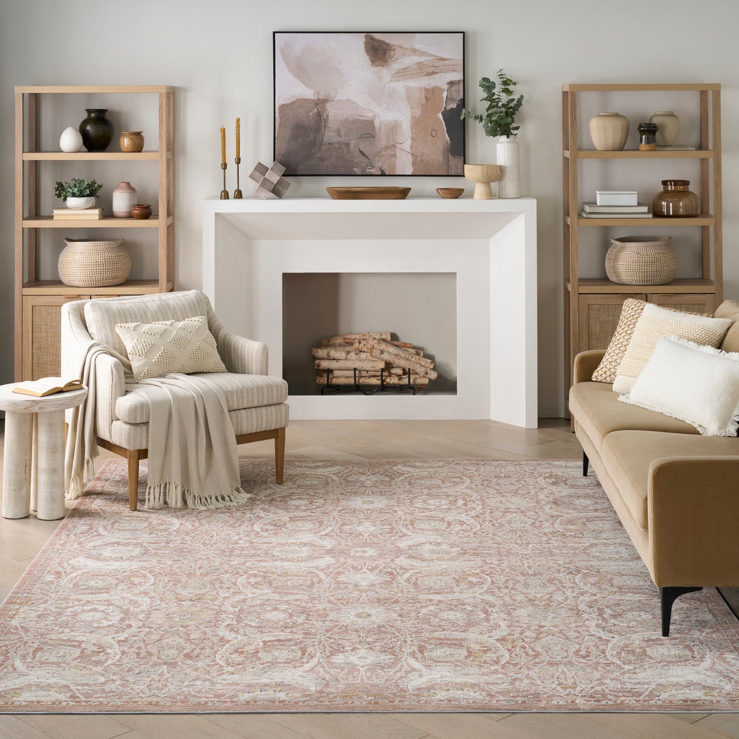 Neutral living room with white fireplace, abstract art, beige sofa, cream armchair, light wood shelves, pale pink rug.