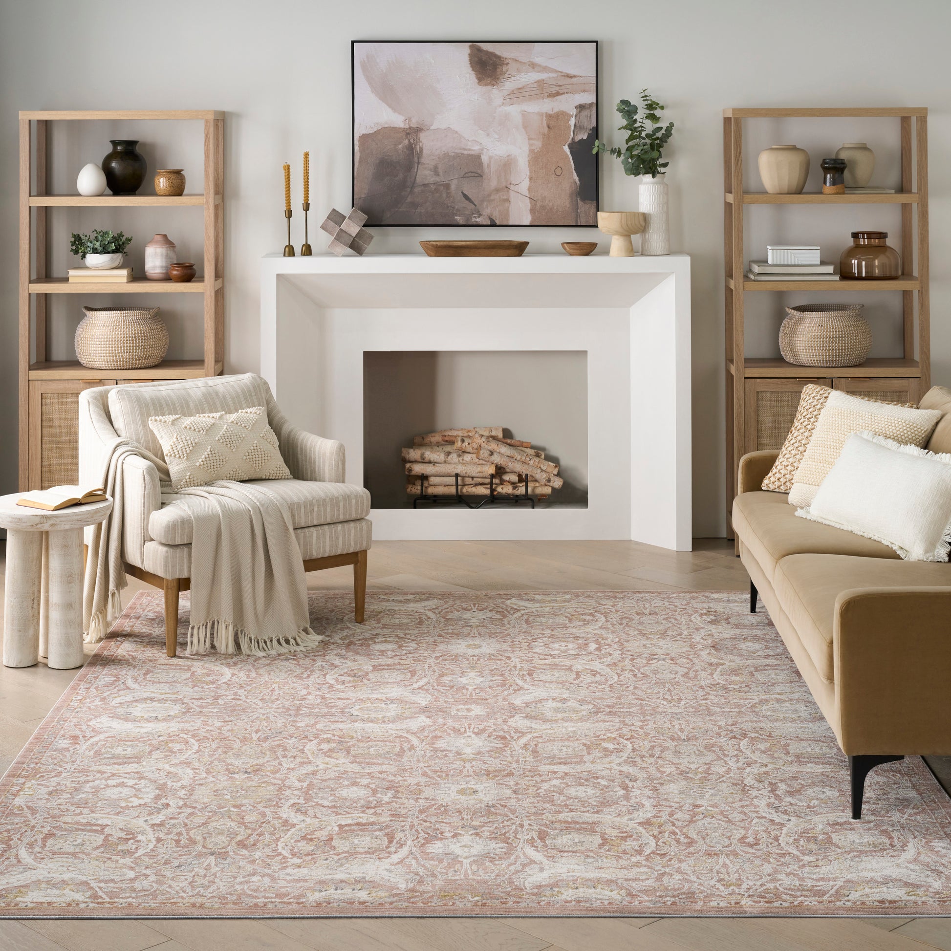Neutral living room with white fireplace, abstract art, beige sofa, cream armchair, light wood shelves, pale pink rug.