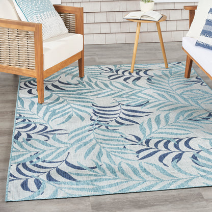 Blue, teal, and navy tropical leaf rug in an outdoor seating area with wooden-framed chairs and a round side table.