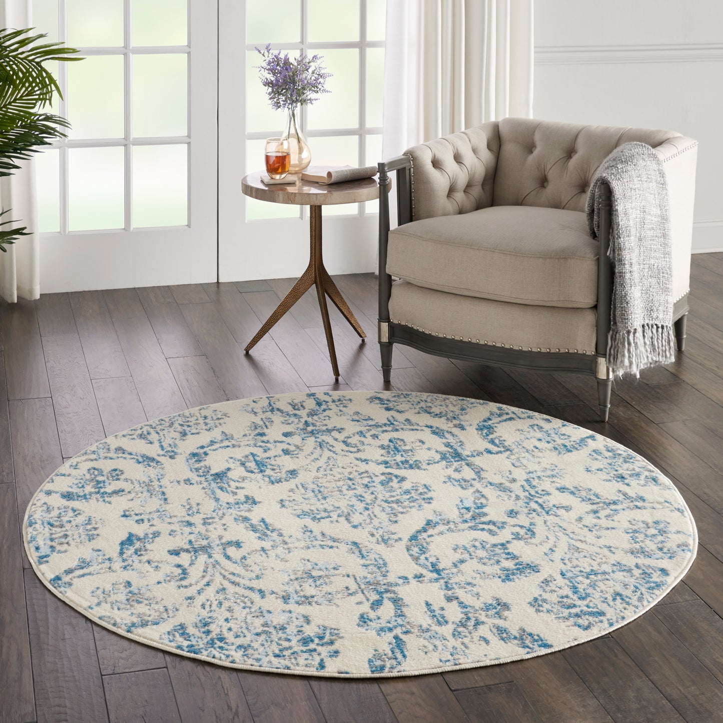 Round beige and blue floral area rug in a cozy living room beside a tufted beige armchair and wooden side table.