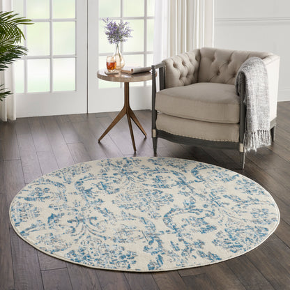 Round beige and blue floral area rug in a cozy living room beside a tufted beige armchair and wooden side table.