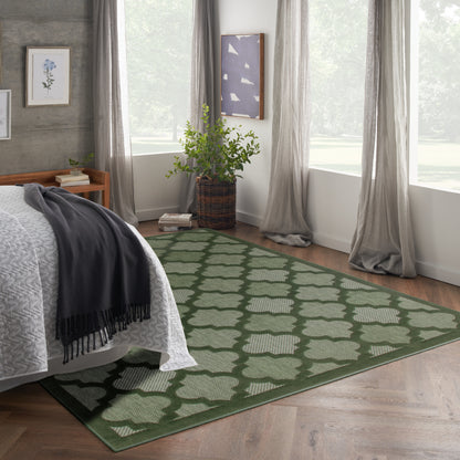 Bedroom with green geometric rug on wood floor, bed with white coverlet and dark gray throw, plant in wicker basket.