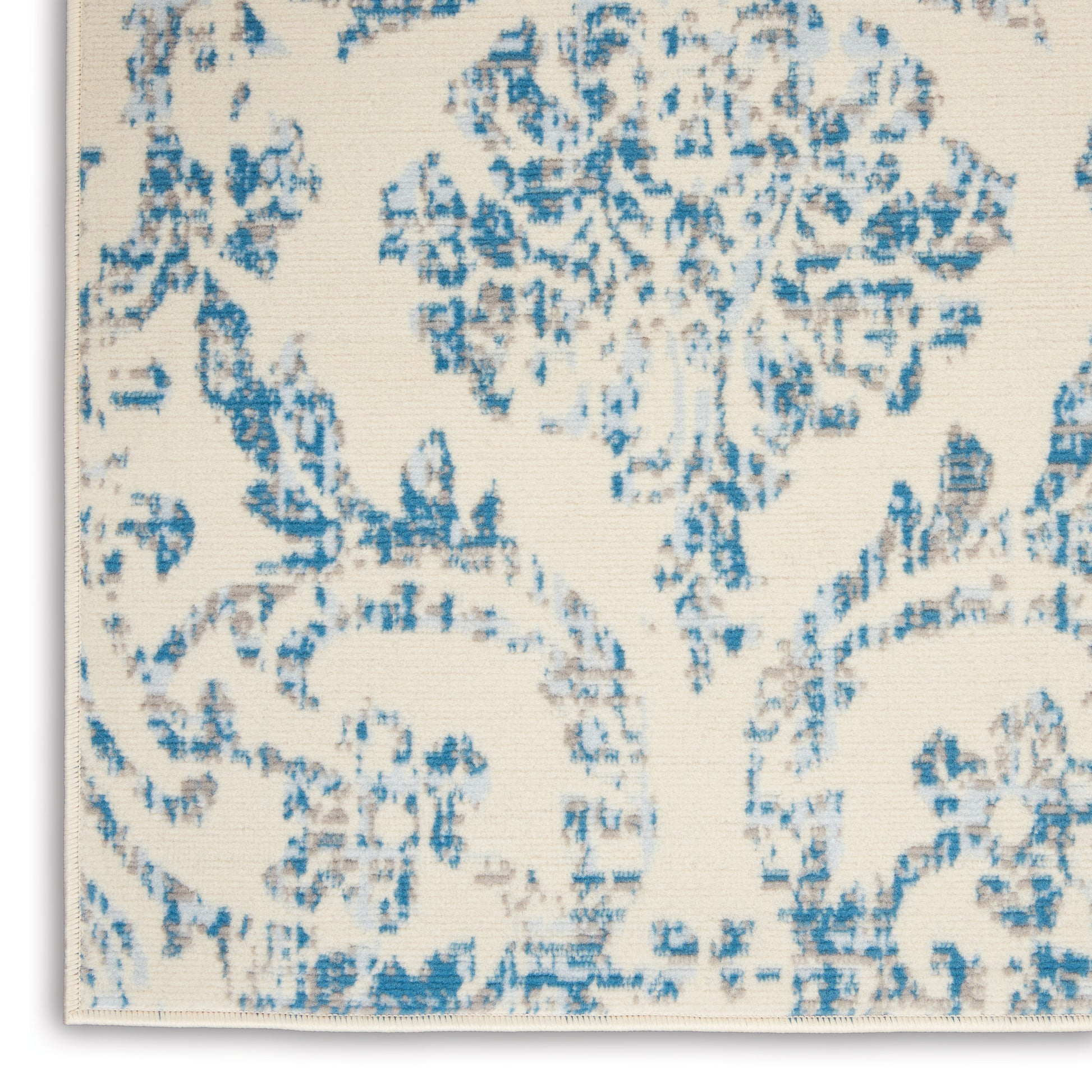 Cream rug with blue damask floral pattern; woven texture.