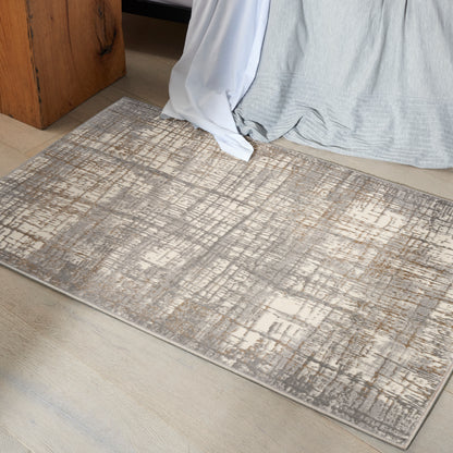 Neutral abstract-pattern area rug in gray and beige on light wood floor beside bed with draped gray and white linens.