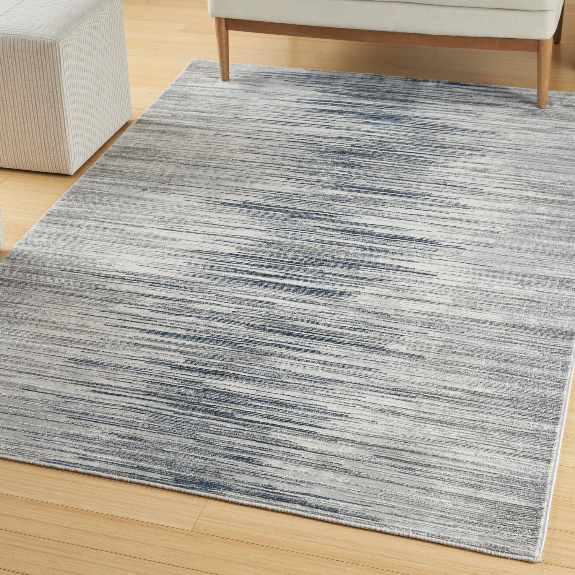Rectangular gray-blue striped area rug on light wood floor in a living room, with sofa legs visible.