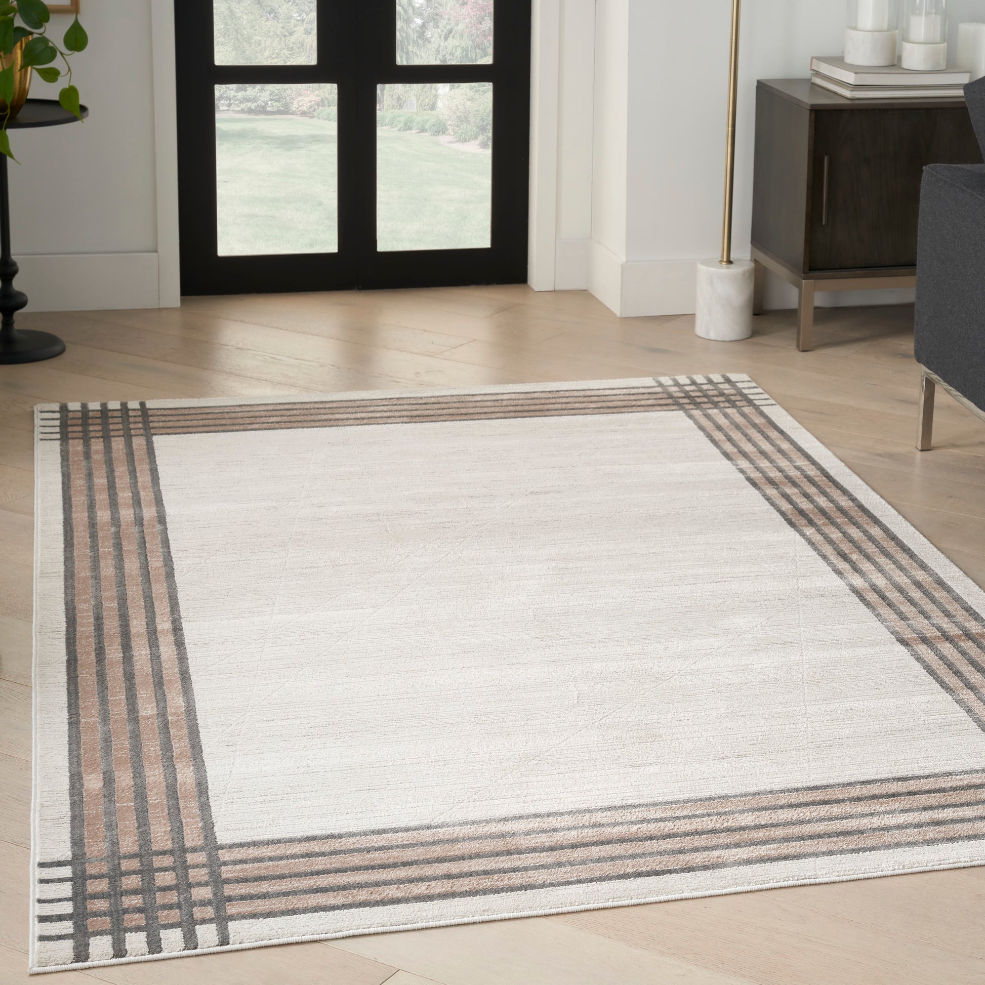 Rectangular beige area rug with brown and gray striped border in a modern living room foyer.