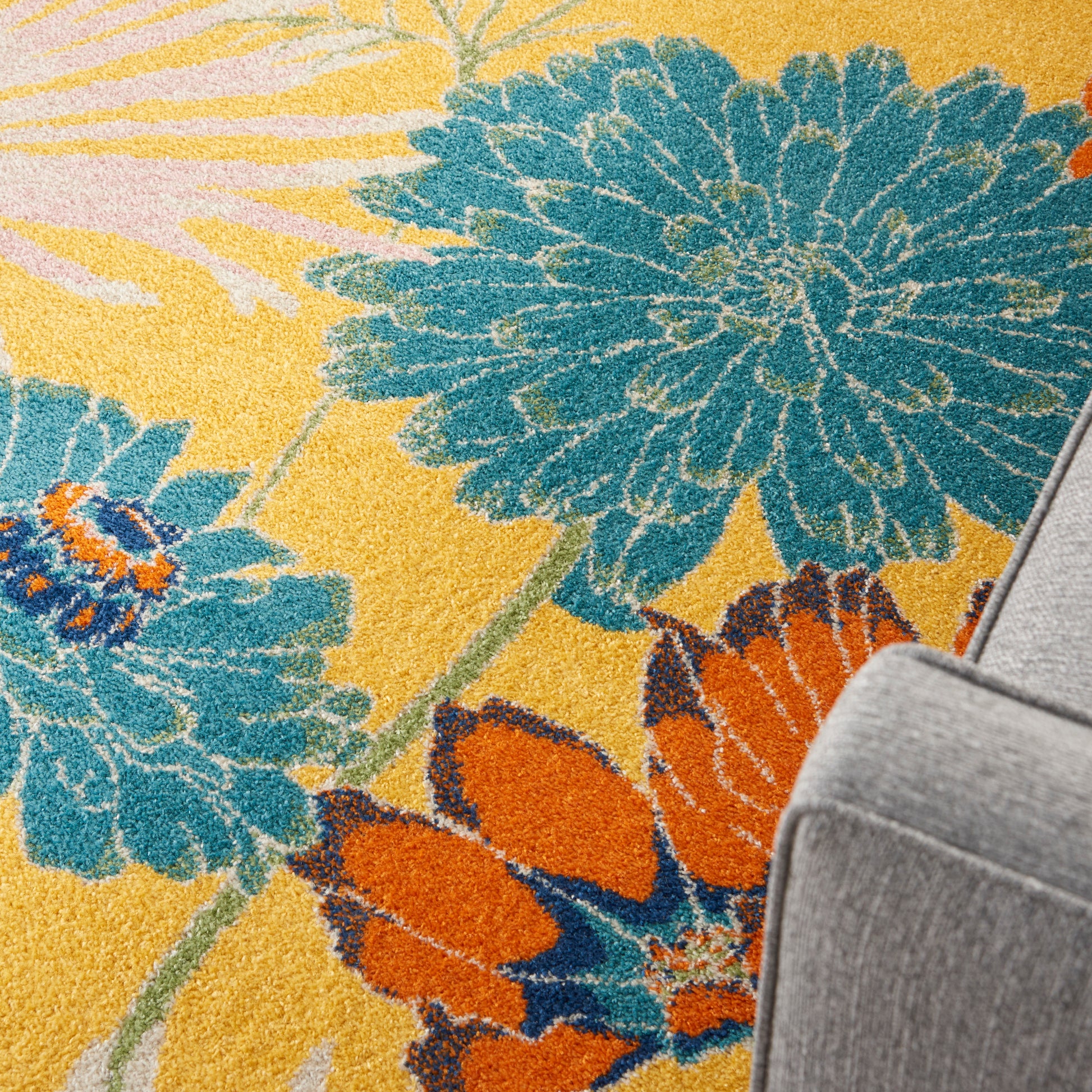 Yellow rug with large teal-blue flowers and orange petals beside a gray sofa.