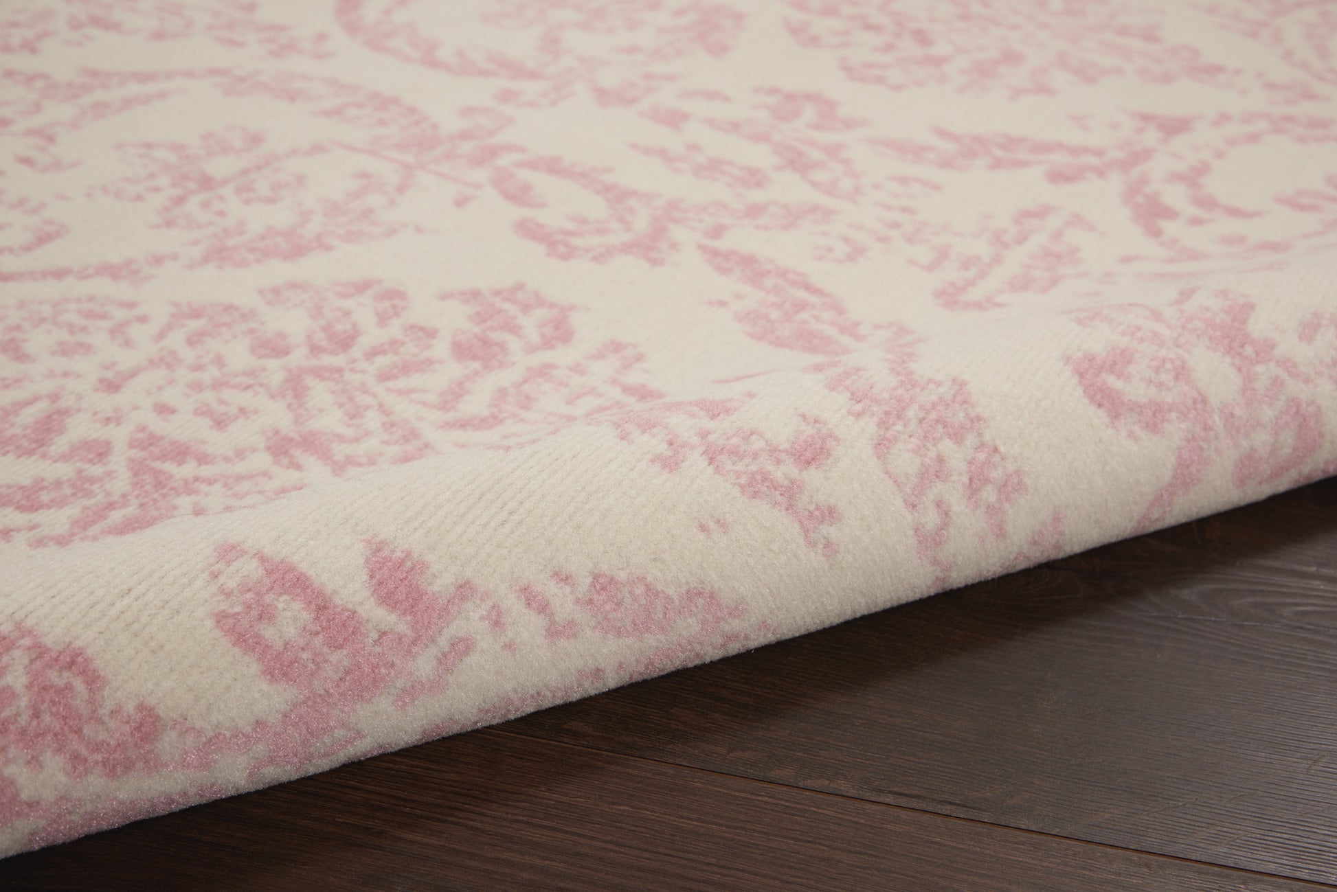 Cream rug with pink damask pattern, soft woven textile on dark wood floor.