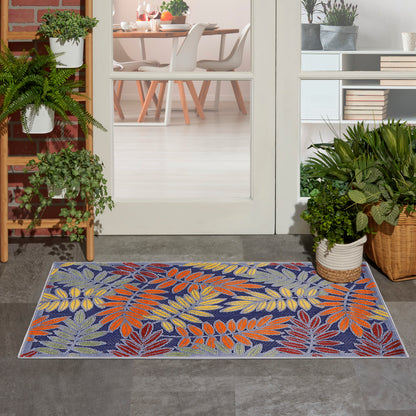 Outdoor rug with a tropical leaf pattern in orange, yellow, and purple on a blue background at a doorway with potted plants.