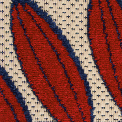 Woven rug close-up with bold red leaf motifs outlined in navy on beige textured background.