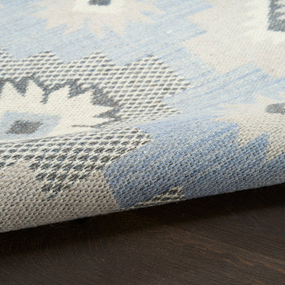 Blue, gray and ivory woven rug with floral motif, folded edge on dark wooden floor.