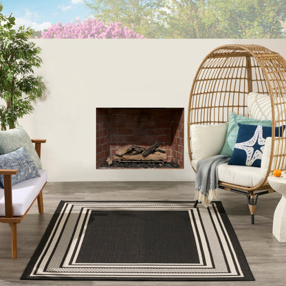 Outdoor patio with brick fireplace, black-and-white striped rug, wicker dome chair & cushions, wooden armchair, potted plant.