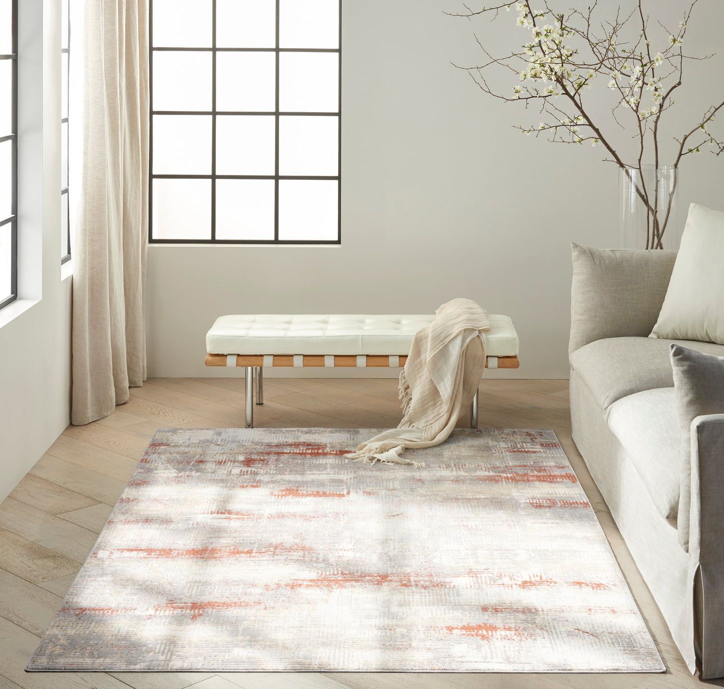Neutral abstract area rug with peach and gray tones in a bright modern living room, paired with a cream bench and gray sofa.