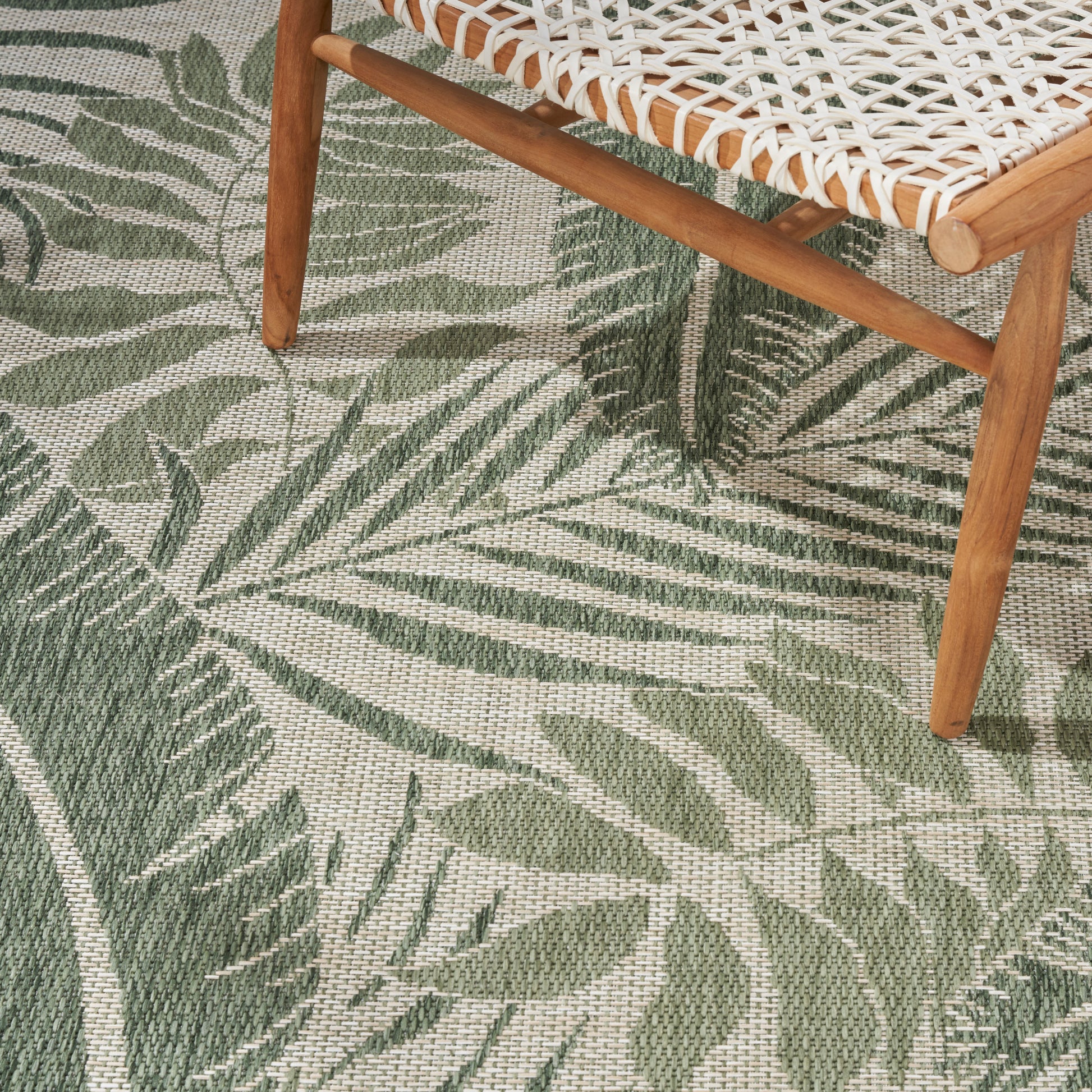 Beige outdoor rug with a green tropical leaf pattern, 10' x 14'.