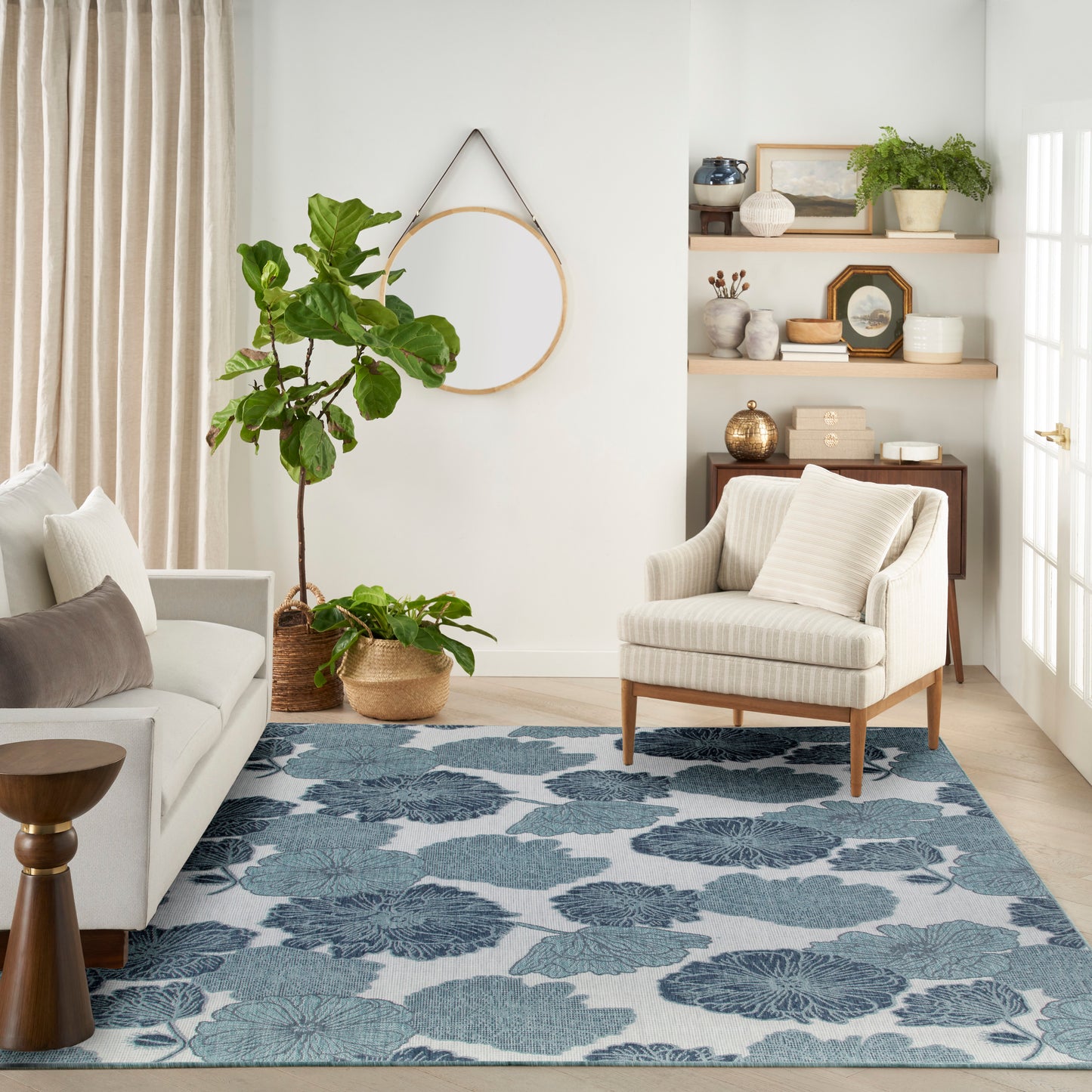 Rectangular blue floral area rug in a bright neutral living room with beige striped armchair, light sofa, and potted plants.